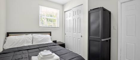 Une chambre à coucher avec un lit, des murs blancs, une fenêtre et une armoire noire.