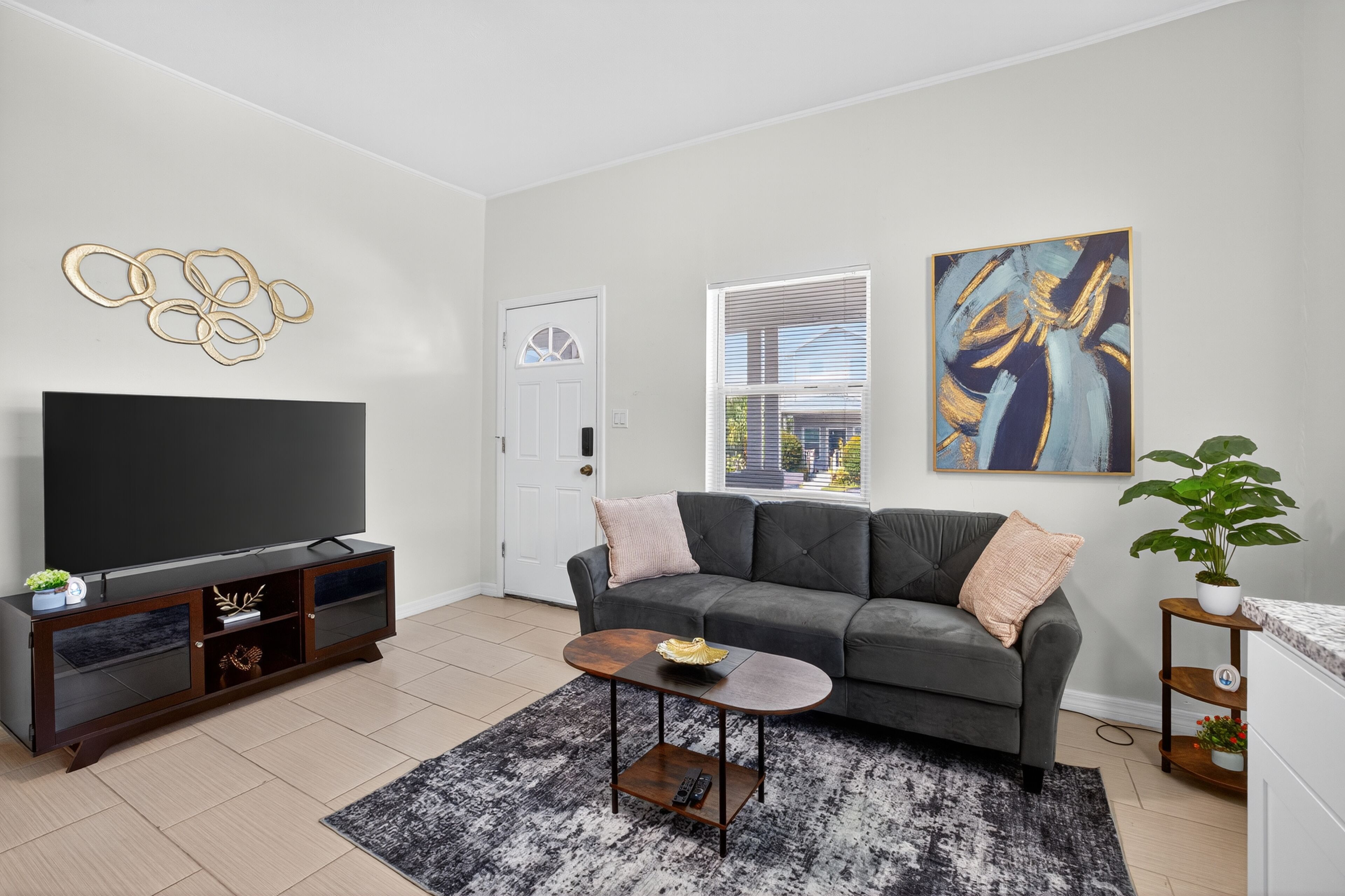 A living room with a dark grey sofa, a flat-screen TV on a wooden cabinet, a coffee table, and a large abstract painting on the wall.