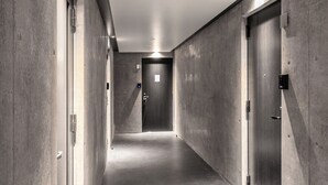 Un couloir aux murs en béton, une porte au fond et un luminaire au plafond.