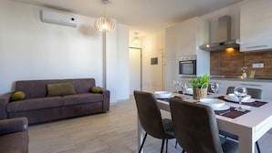 Un salon moderne avec un canapé, une table à manger dressée avec des assiettes et des verres, et un coin cuisine équipé d’une cuisinière et de placards.