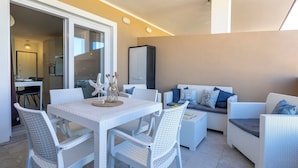 Un espace de vie moderne comprenant une table à manger, des meubles en osier blancs et une grande fenêtre.