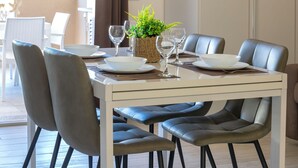 Un coin repas avec une table blanche dressée pour quatre personnes, entourée de chaises grises.