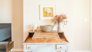 A rustic wooden desk with a woven bowl, a vase with dried flowers, and a framed painting on the wall. - Suffolk House, Saxmundham (Saxmundham)