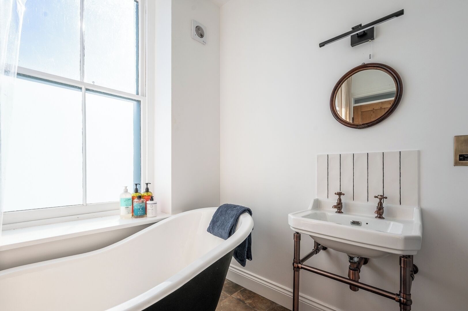 A bathroom with a freestanding bathtub, a white sink with a vintage-style faucet, and a round mirror on the wall.