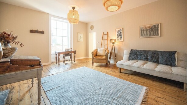 A spacious living room with a wooden floor, a white sofa, a blue rug, and two hanging wicker lamps. - Suffolk House, Saxmundham (Saxmundham)