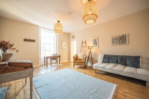 A spacious living room with a wooden floor, a white sofa, a blue rug, and two hanging wicker lamps. - Suffolk House, Saxmundham (Saxmundham)