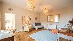 A cozy living room with a wooden floor, a white sofa, a small table with a chair, and a ladder leaning against the wall. - Suffolk House, Saxmundham (Saxmundham)