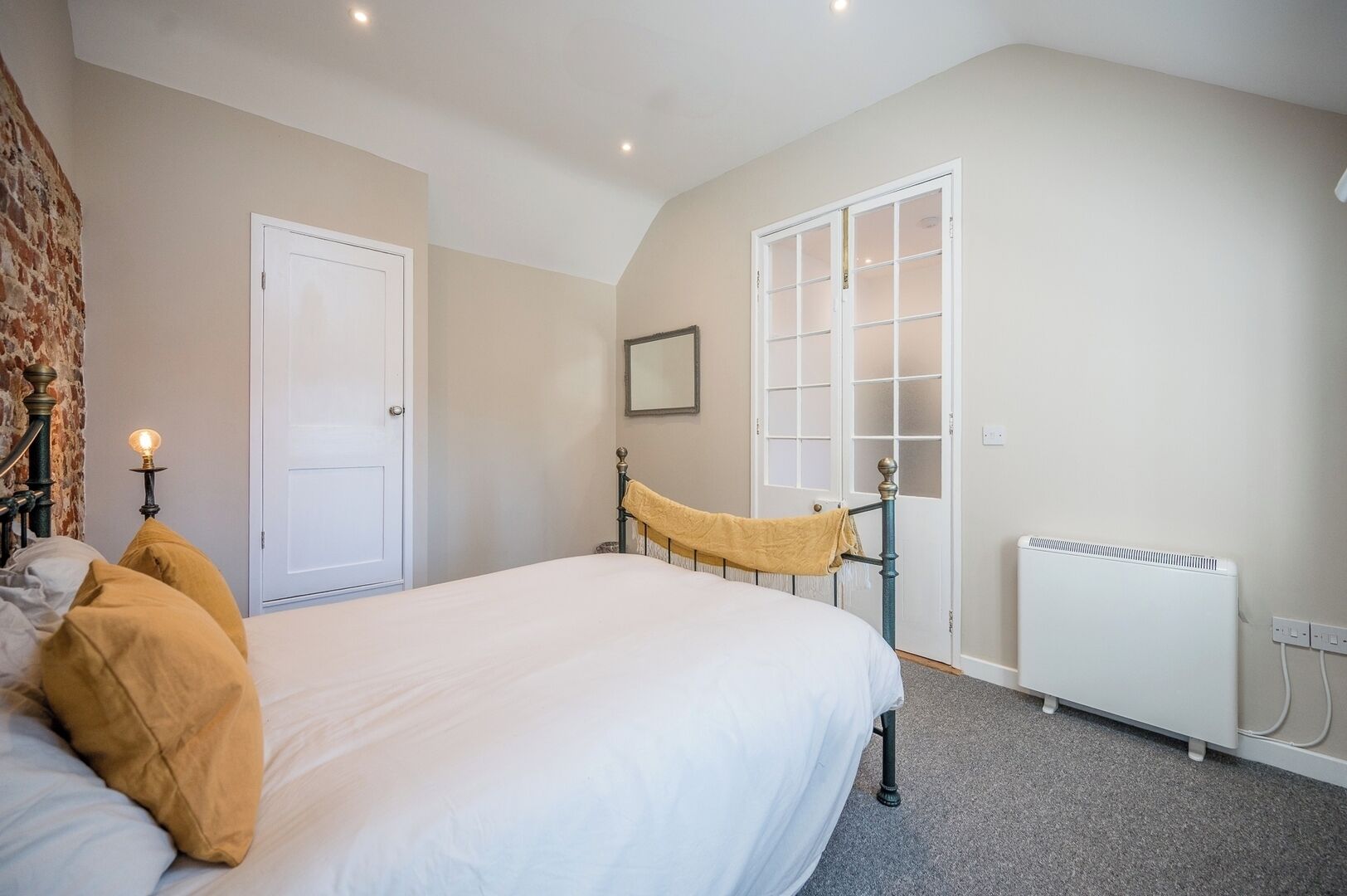 Un dormitorio con cama, una puerta blanca, una ventana, un radiador y una lámpara.