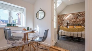 A cozy room with a dining area featuring a round table and chairs, a brick wall, and a bed with a yellow blanket. - Suffolk House, Saxmundham (Saxmundham)