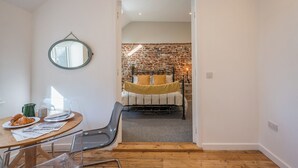 A room with a bed, a dining table with chairs, a mirror, and a brick wall. - Suffolk House, Saxmundham (Saxmundham)