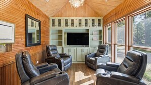 Ein gemütliches Zimmer mit Holzwänden, einer Kristallleuchtre, einem großen Flachbildfernseher und Ledersesseln.