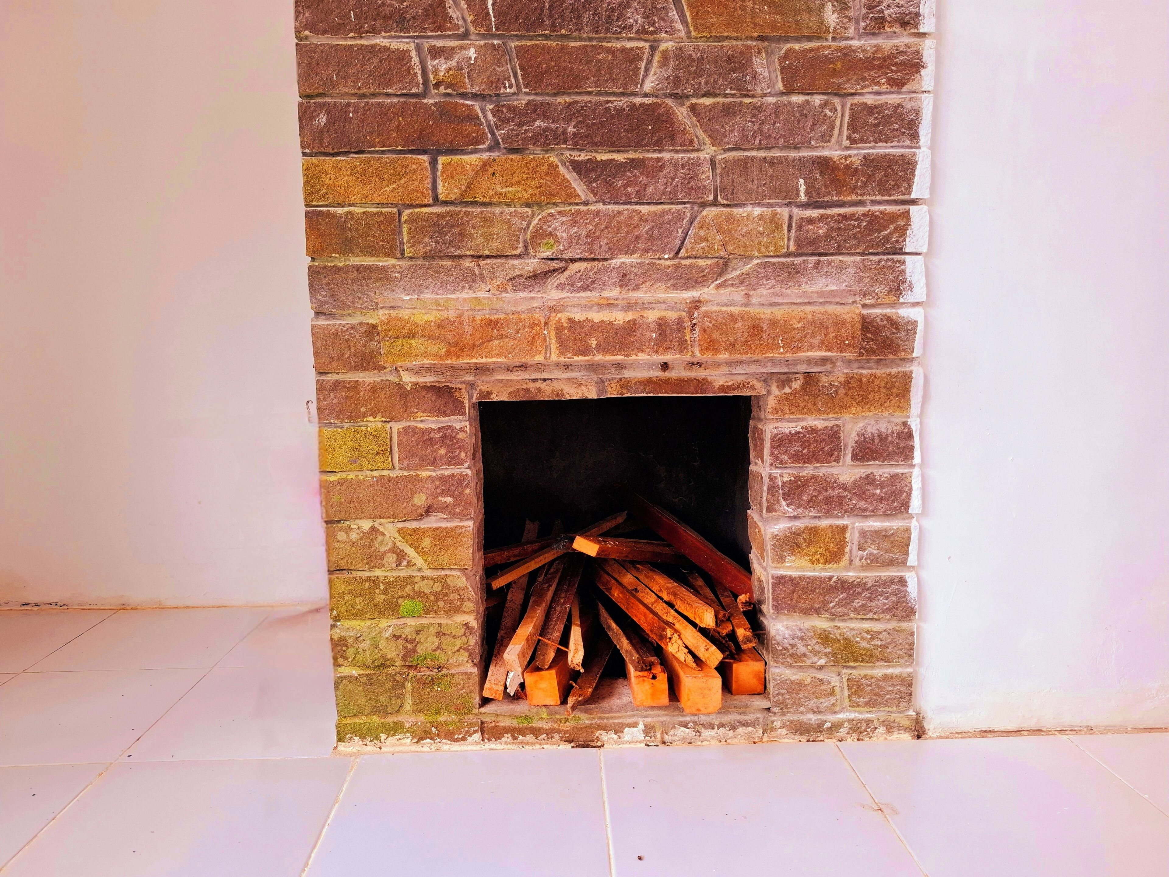 A stone fireplace with a firebox, surrounded by white walls and a tiled floor.