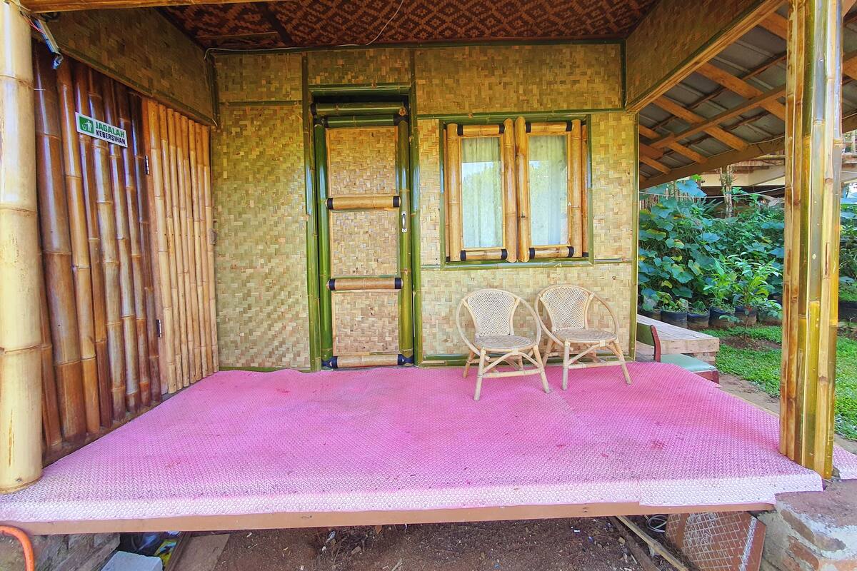 A room with a bamboo wall, a wooden door, two wicker chairs, and a pink mat on the floor.