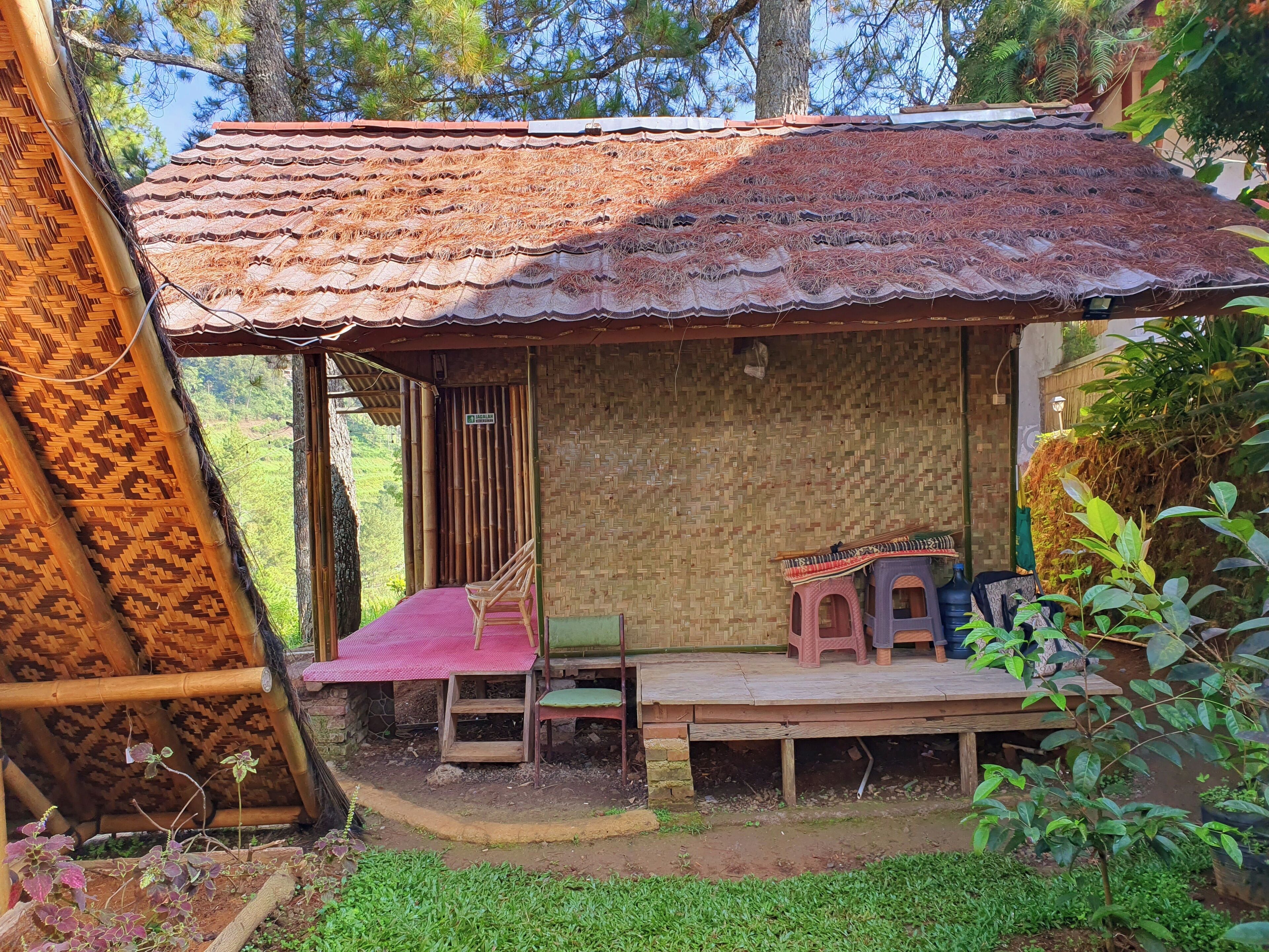 A rustic wooden structure with a tiled roof, a small porch with a bench, and a bamboo wall.