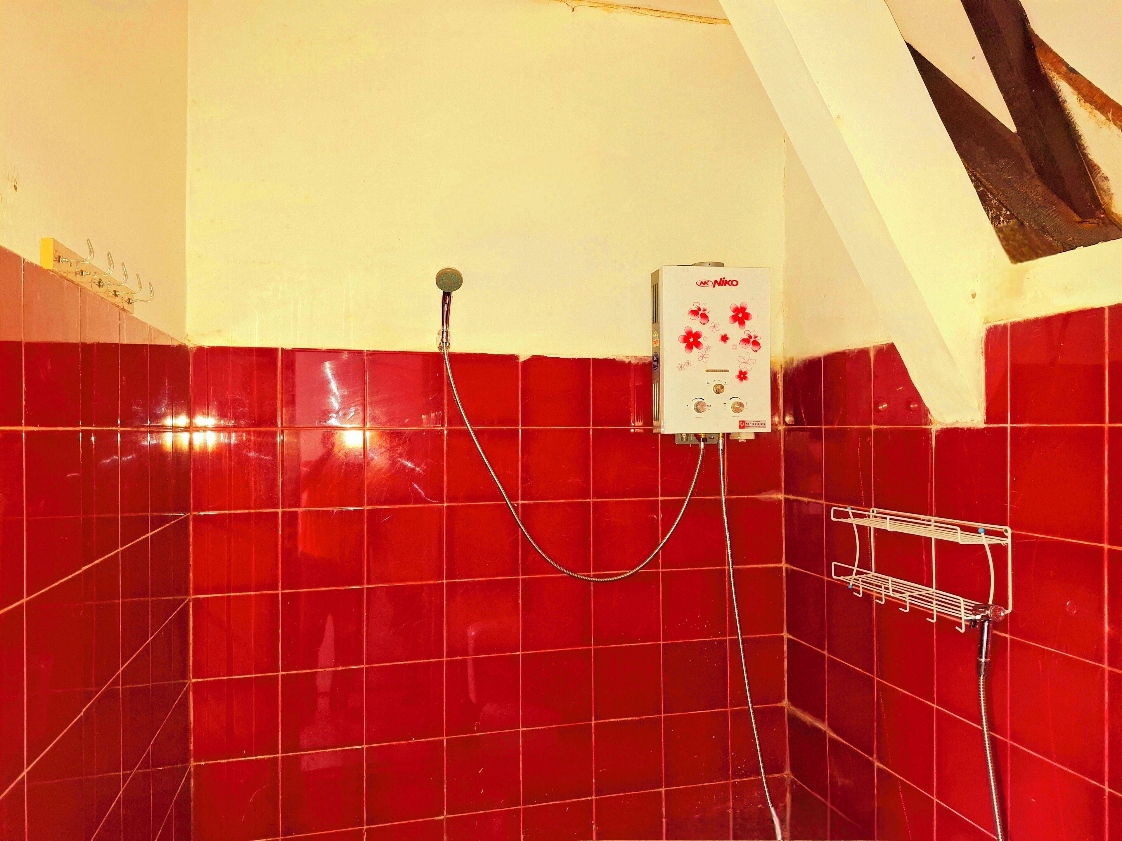A shower area with red tiles, a white wall, and a ceiling with a triangular design.