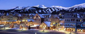 Une ville de montagne enneigée, au crépuscule, avec des bâtiments illuminés et des sapins de Noël.