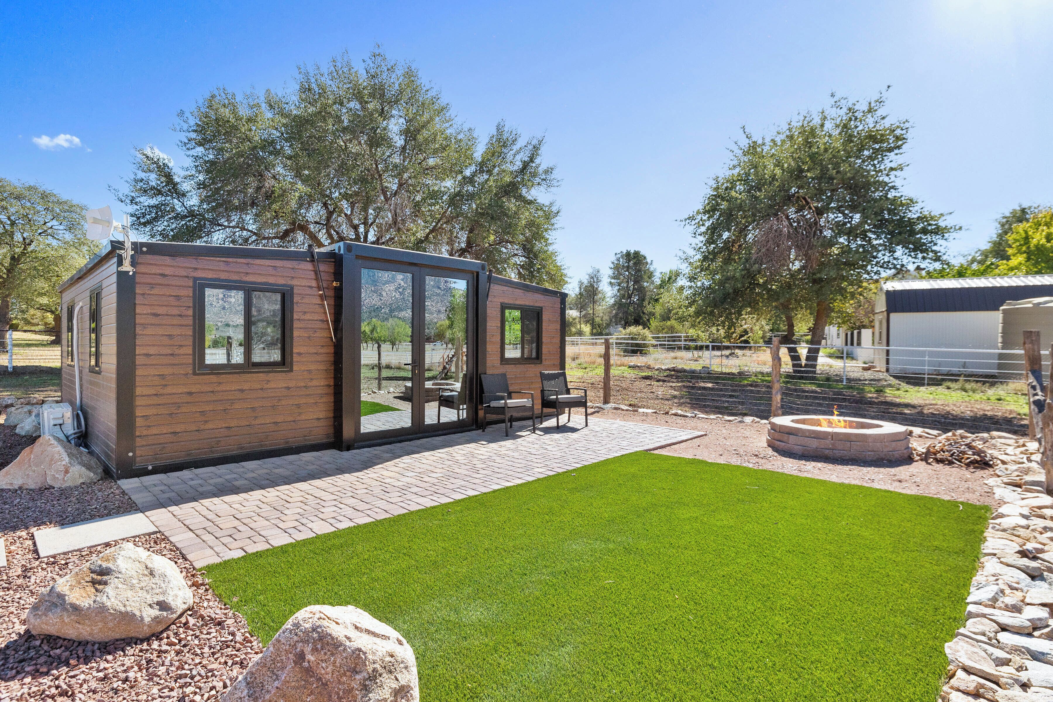 A modern outdoor living area with a wooden structure, a fire pit, and a well-maintained lawn.