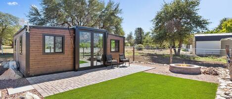 A modern outdoor living area with a wooden structure, a fire pit, and a well-maintained lawn.