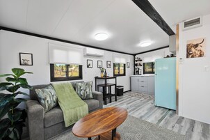 Una sala de estar moderna con un sofá gris, una mesa de centro de madera y una zona de cocina con un refrigerador azul claro.