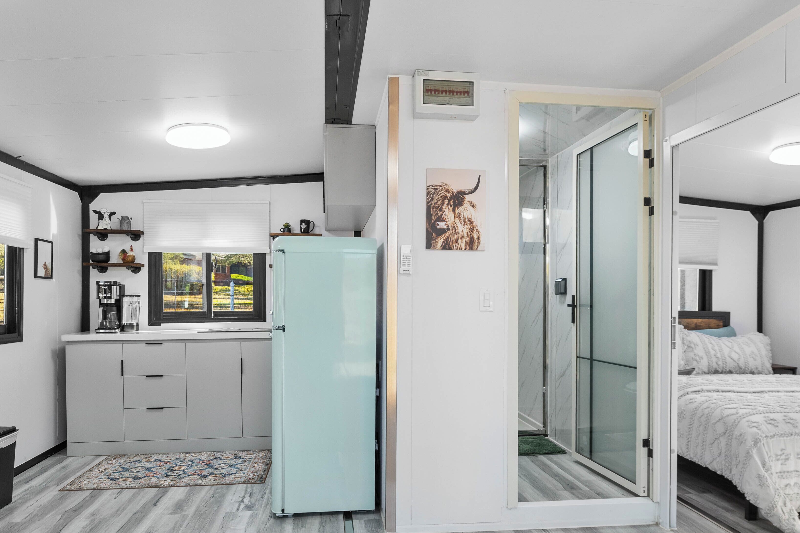 Una habitación de hotel compacta con kitchenette, una puerta corrediza de vidrio a un balcón y una cama con cubrecama blanco.