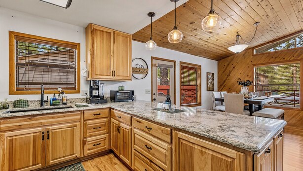 A spacious kitchen with wooden cabinets, a granite countertop, and pendant lighting.
