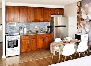 A kitchen with wooden cabinets, a stainless steel refrigerator, a stove, and a dining area with a table and chairs. - Free Parking Newly Renovated 12th FL Great View (Honolulu)