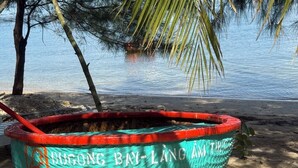 A woven basket with the text "DUGONG BAY-LANG AM THU" on a sandy beach near water. - Cay Sao Beach Glamping Phu Quoc (Phu Quoc)