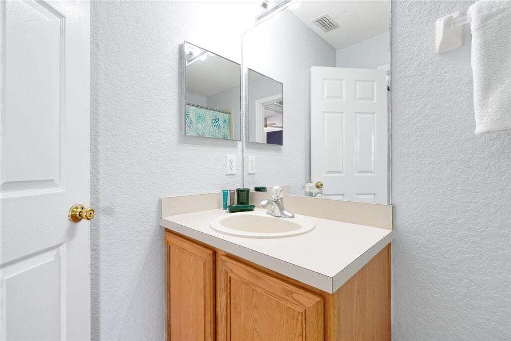 A bathroom with a white sink, wooden cabinets, a mirror, and a white door.