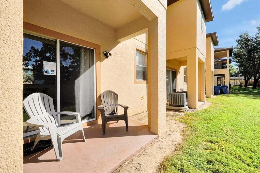 A building with a covered patio area, two chairs, and a small lawn.