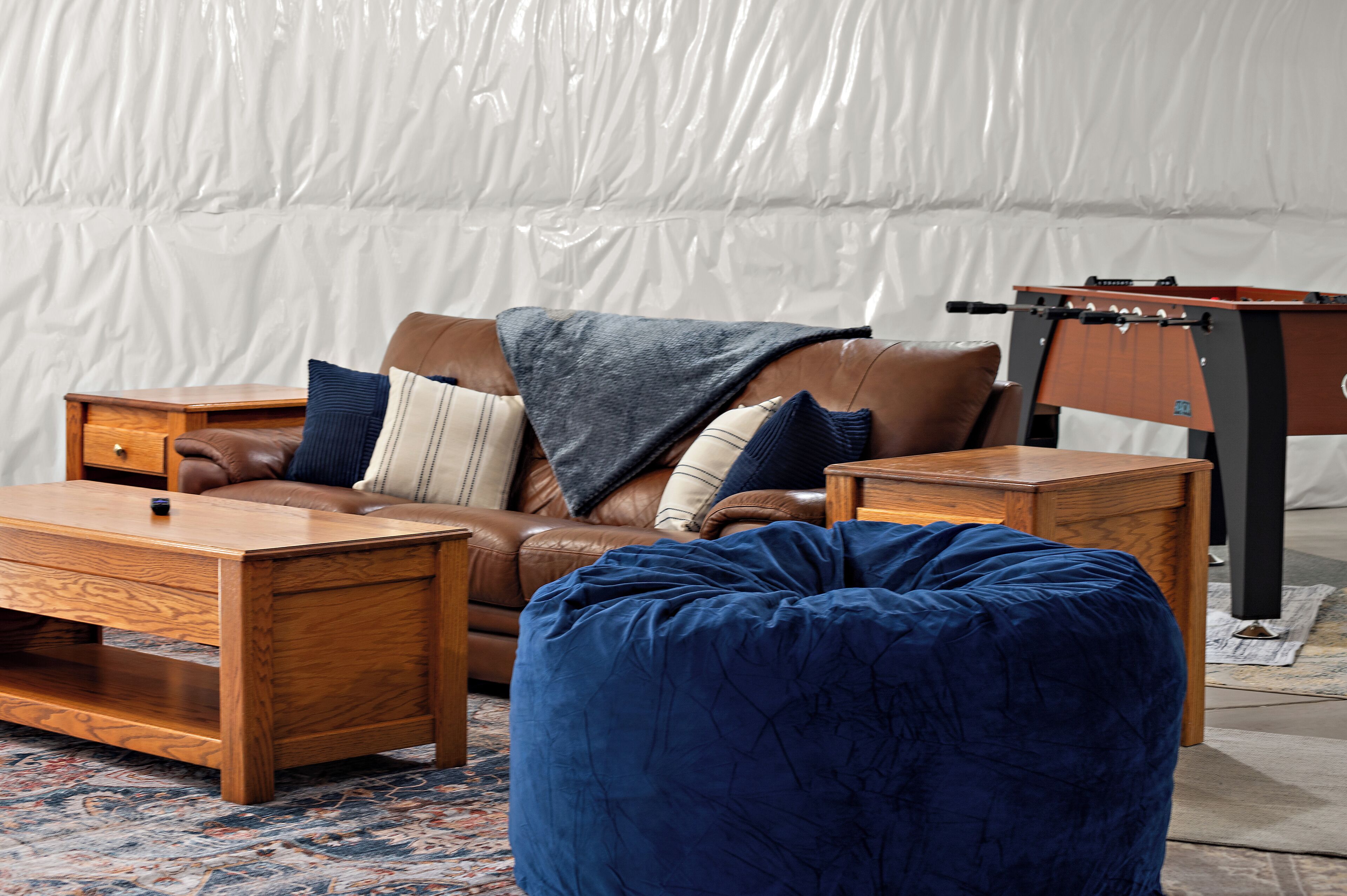 Un salon avec un canapé en cuir marron, un pouf bleu, une table basse en bois et une petite table d’appoint en bois.