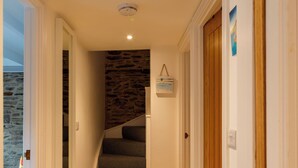 A staircase with a stone wall behind it, leading to a room with a wooden door and a small painting on the wall. - Shanty Cottage by Interhome (Mevagissey)