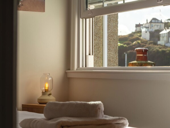A bedroom with a window, a bedside lamp, and a neatly folded towel on the bed.