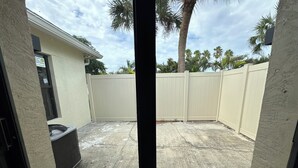 Ein Garten mit einem beigefarbenen Zaun, einer überdachten Terrasse und einer Palme.