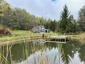 Ein Haus mit einem Steg, der in einen Teich führt, umgeben von Bäumen und einer Wiese.