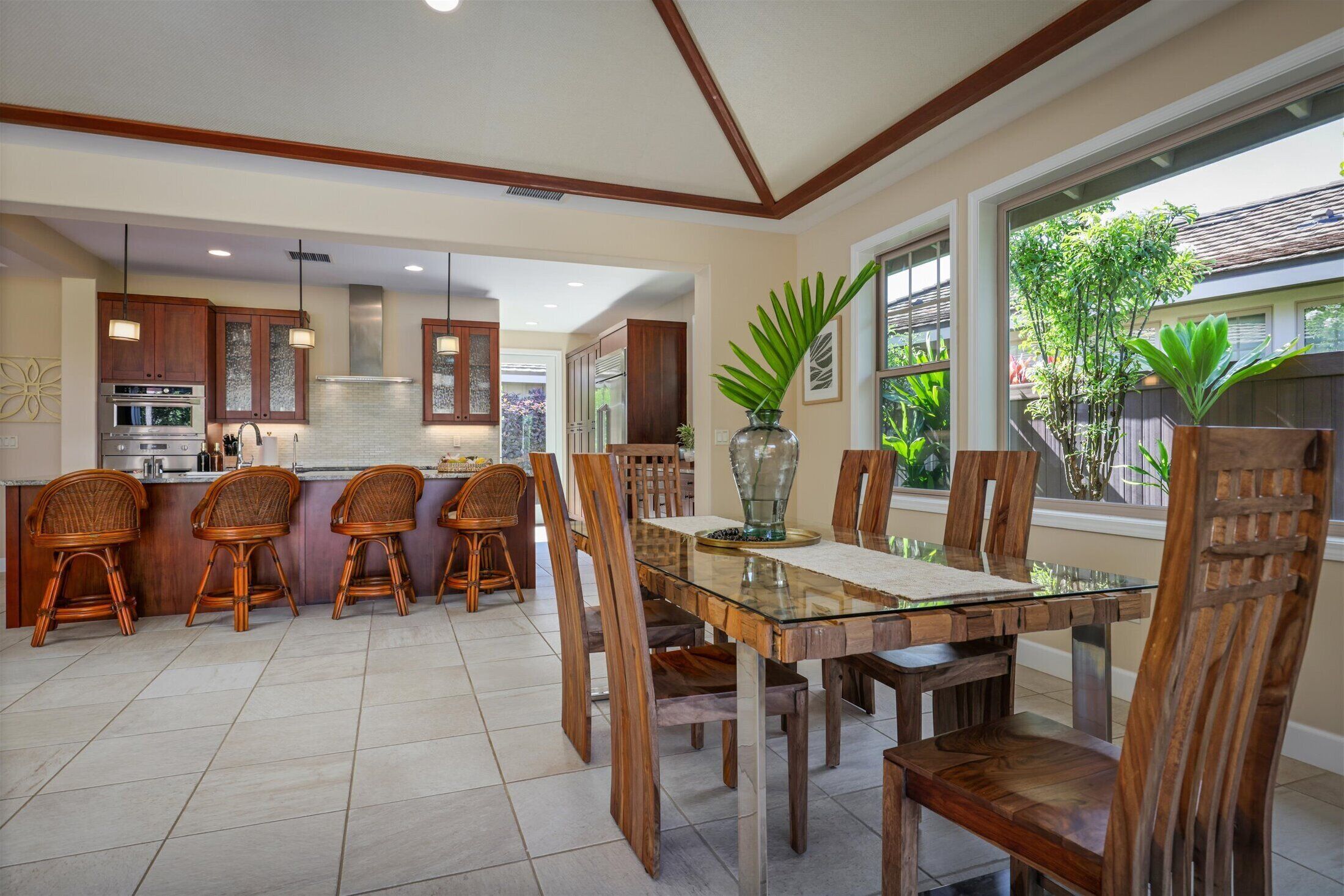 A modern kitchen with wooden cabinets, a glass dining table, and wicker chairs.