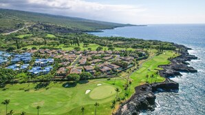 An aerial view of a coastal resort with multiple bungalow-style accommodations, a golf course, and a rocky shoreline.