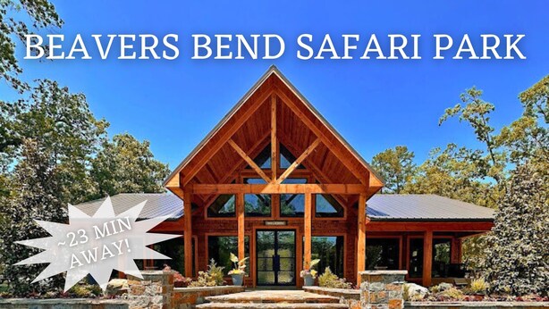 Een lodge met een opvallende houten constructie en een stenen ingang, aangeduid als Beavers Bend Safari Park, met een bord waarop staat dat de rit 23 minuten duurt.