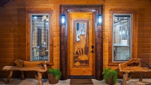 A wooden cabin entrance with a carved wolf door, two benches, and potted plants.