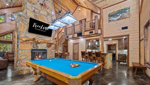 A spacious room with a pool table, a stone fireplace, and a wooden ceiling.