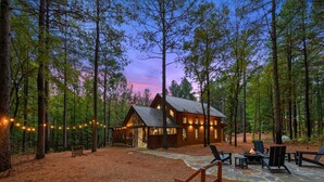 A cabin with a stone patio, outdoor seating, and string lights in a forest setting.
