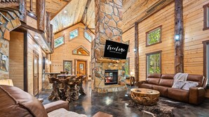 A spacious log cabin interior with a stone fireplace, leather furniture, and a stone wall accent.
