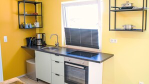 A compact kitchen with a built-in oven, a sink, and a window with blinds.