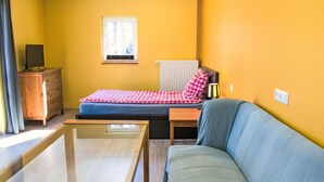 A compact room with a bed, a sofa, a wooden dresser, and a window.
