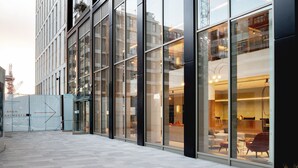 Ein modernes Gebäude mit großen Glasfenstern, ein Innenhof mit Fliesenboden und ein Schild mit der Aufschrift 'Show Apartments'.