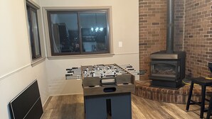Una sala de estar acogedora con una mesa de fútbol de mesa, una chimenea y una ventana con vistas a la ciudad.