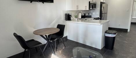 Una cucina moderna con mobili bianchi, forno a microonde integrato e frigorifero in acciaio inossidabile. C'è un'area pranzo con un tavolo rotondo e due sedie.
