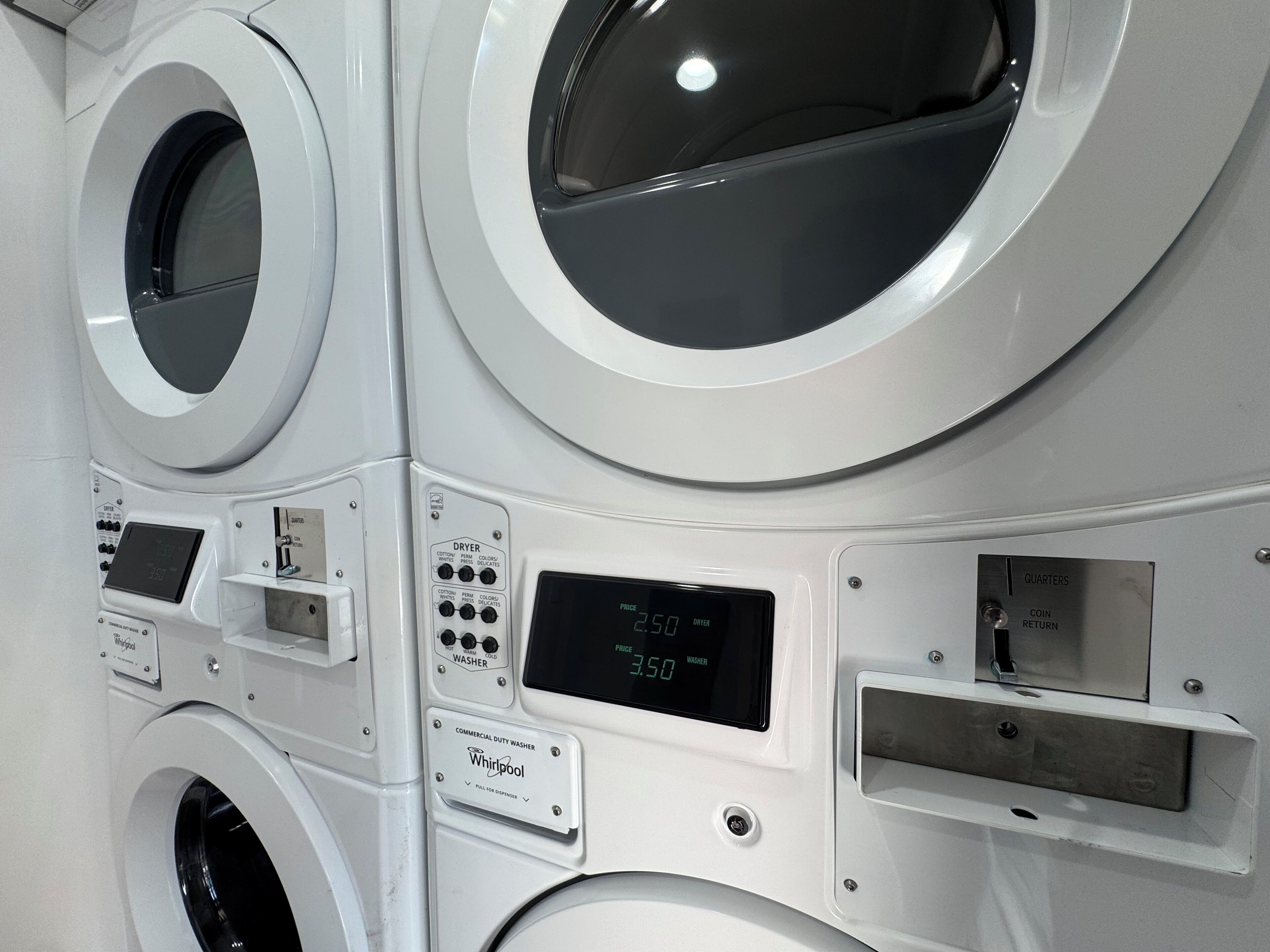 Een wasserette met meerdere wasmachines, bedieningspanelen en een digitaal scherm dat prijzen toont.