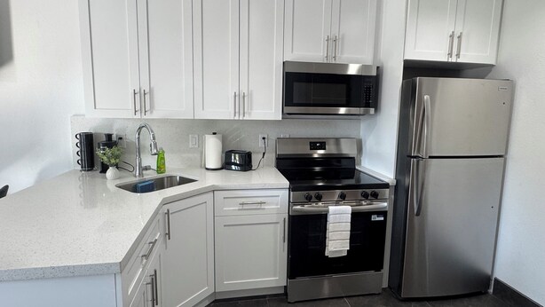 A modern kitchen with white cabinets, a stainless steel refrigerator, a microwave, a stove, and a dishwasher. - Clewiston Comfort #4 – Stylish 1BR Hideaway (Clewiston)