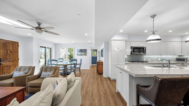 A modern kitchen with a large island, white cabinetry, and a microwave. There is a dining area with a table and chairs, and a ceiling fan. - Charming 3-bedroom house in lovely San Clemente with AC, Walk to the Pier! (San Clemente)