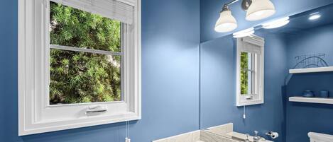 Un bagno con una parete blu, un mobile lavabo bianco con lavandino, uno specchio e una finestra con persiane.